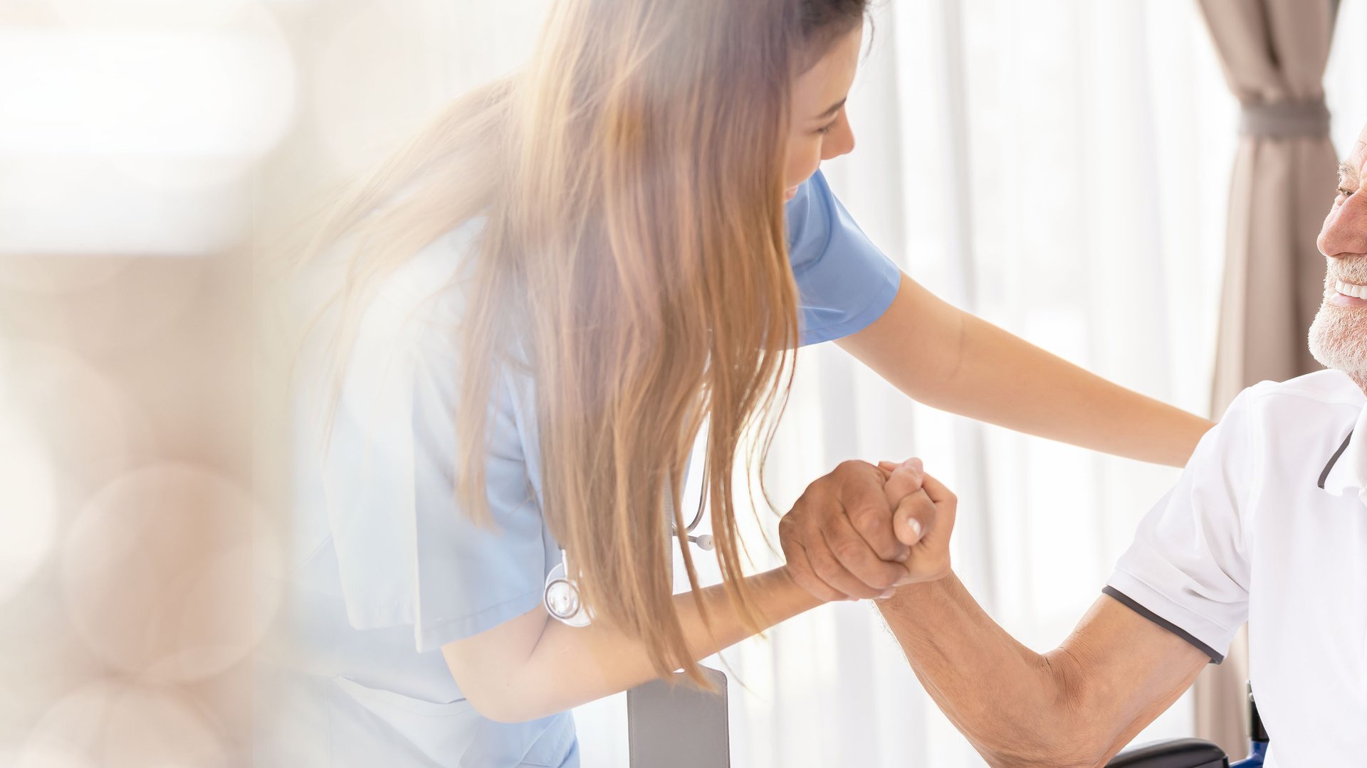 A nurse warmly holding hands with a smiling senior man