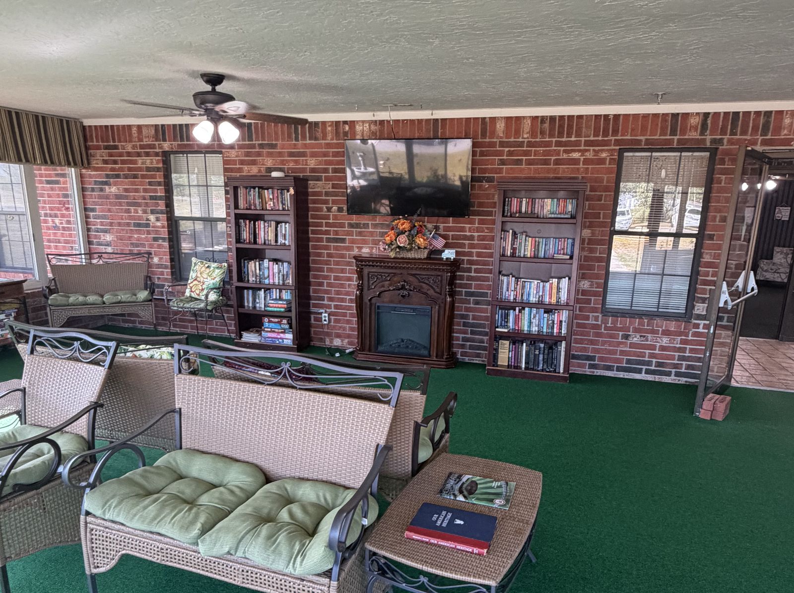 A sunroom with wicker seating, bookshelves and a brick fireplace